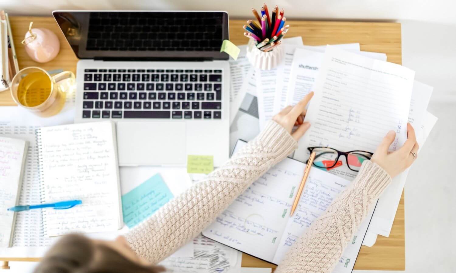 woman's arms holding papers over her mess desk