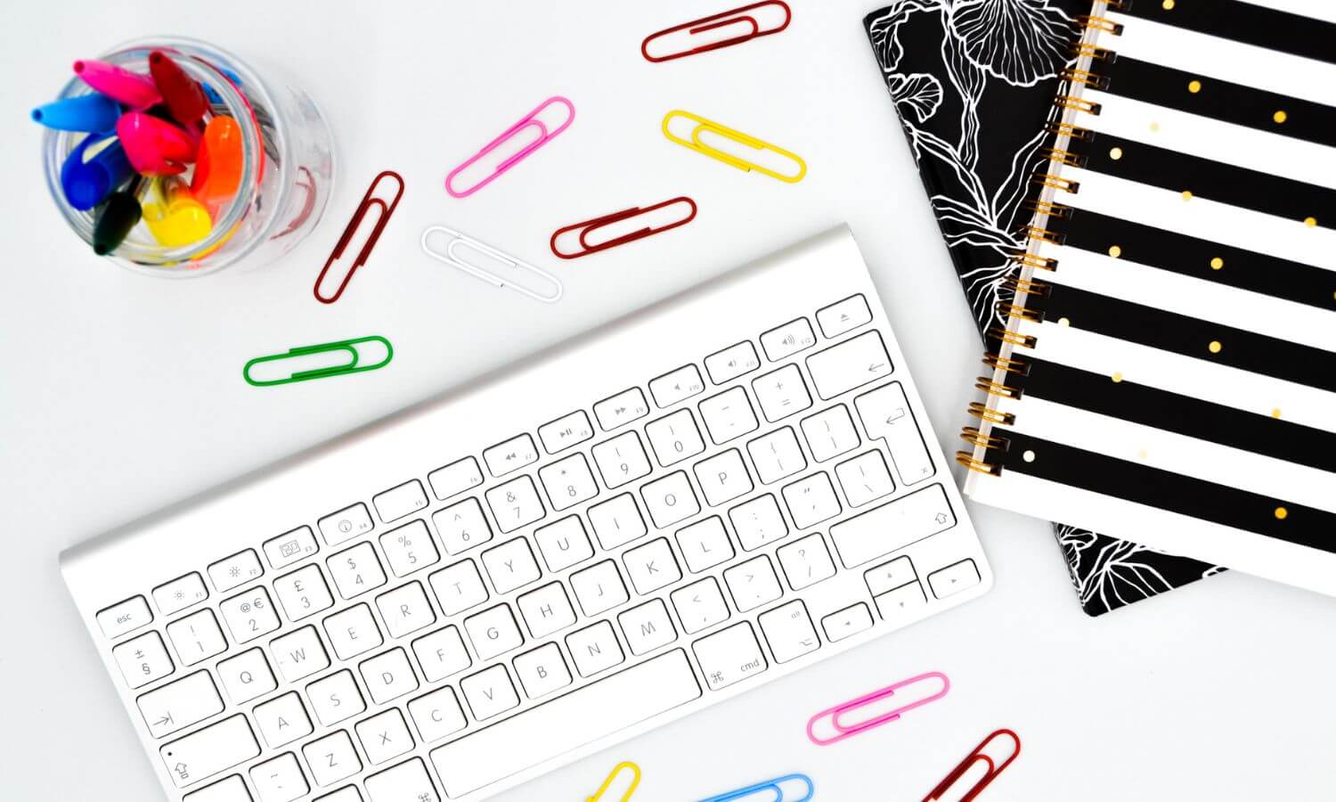 colorful paperclips, white keyboard, and black and white notebooks on a white background