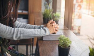 woman's arms with folded hands on top of her Bible