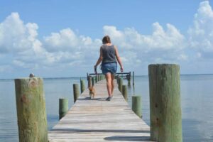 Paula walking Buffy in a pier over the ocean on a sunny day with clouds in the sky